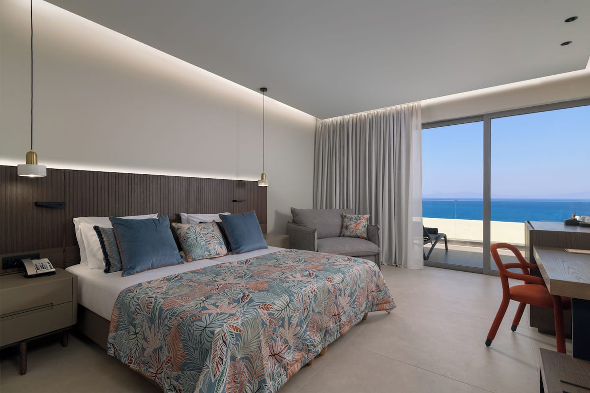 A modern hotel room with a large bed, a desk, and a view of the ocean.