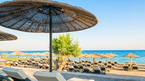 Un complexe hôtelier en bord de mer, avec des rangées de chaises longues et des parasols en chaume.