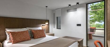 Una habitación de hotel moderna con una cama grande, cabecera de madera, mesita de noche, televisor montado en la pared y una puerta corrediza de cristal que da a un patio exterior.