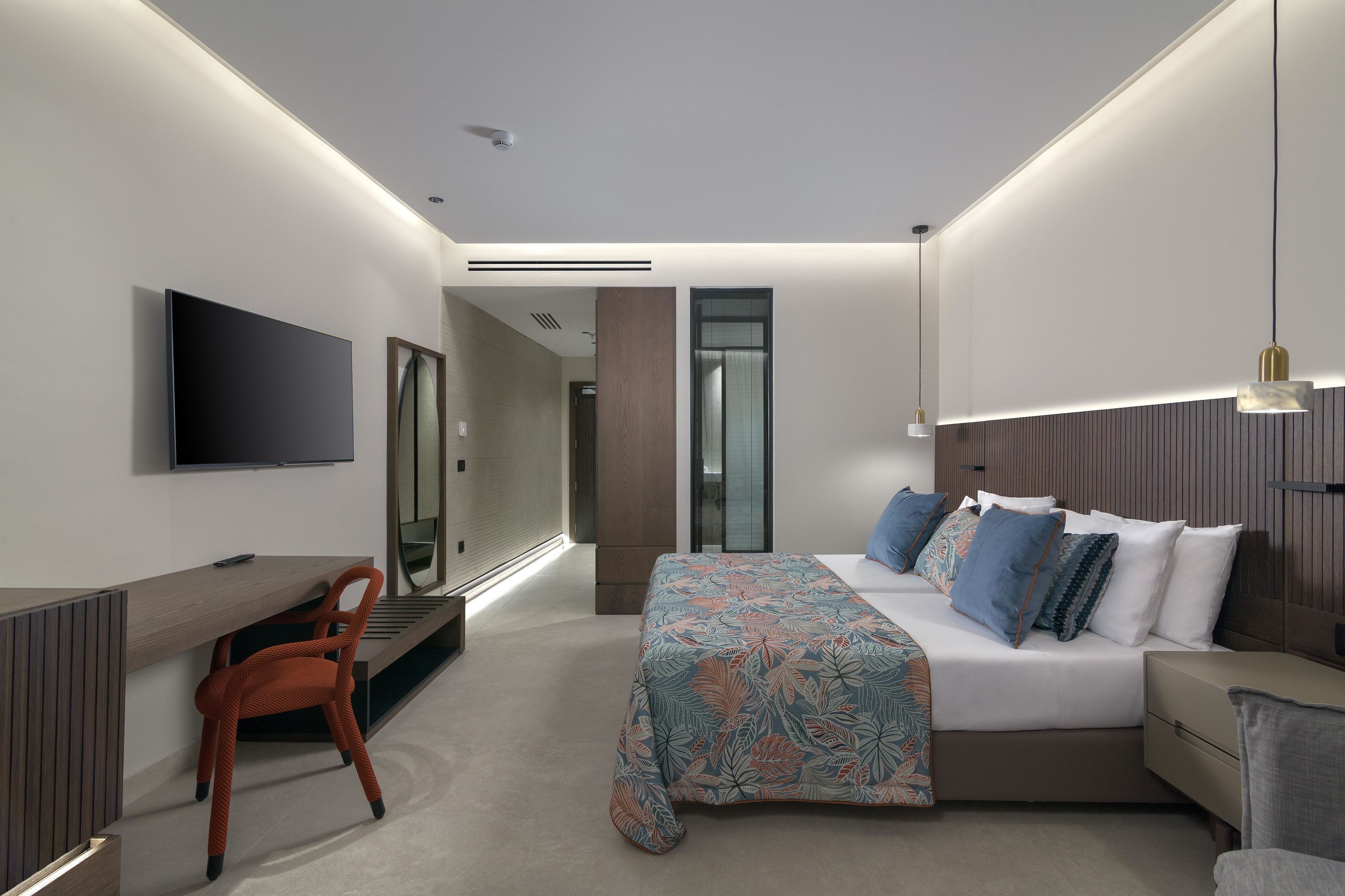 A modern hotel room with a bed, a desk, a chair, and a TV.