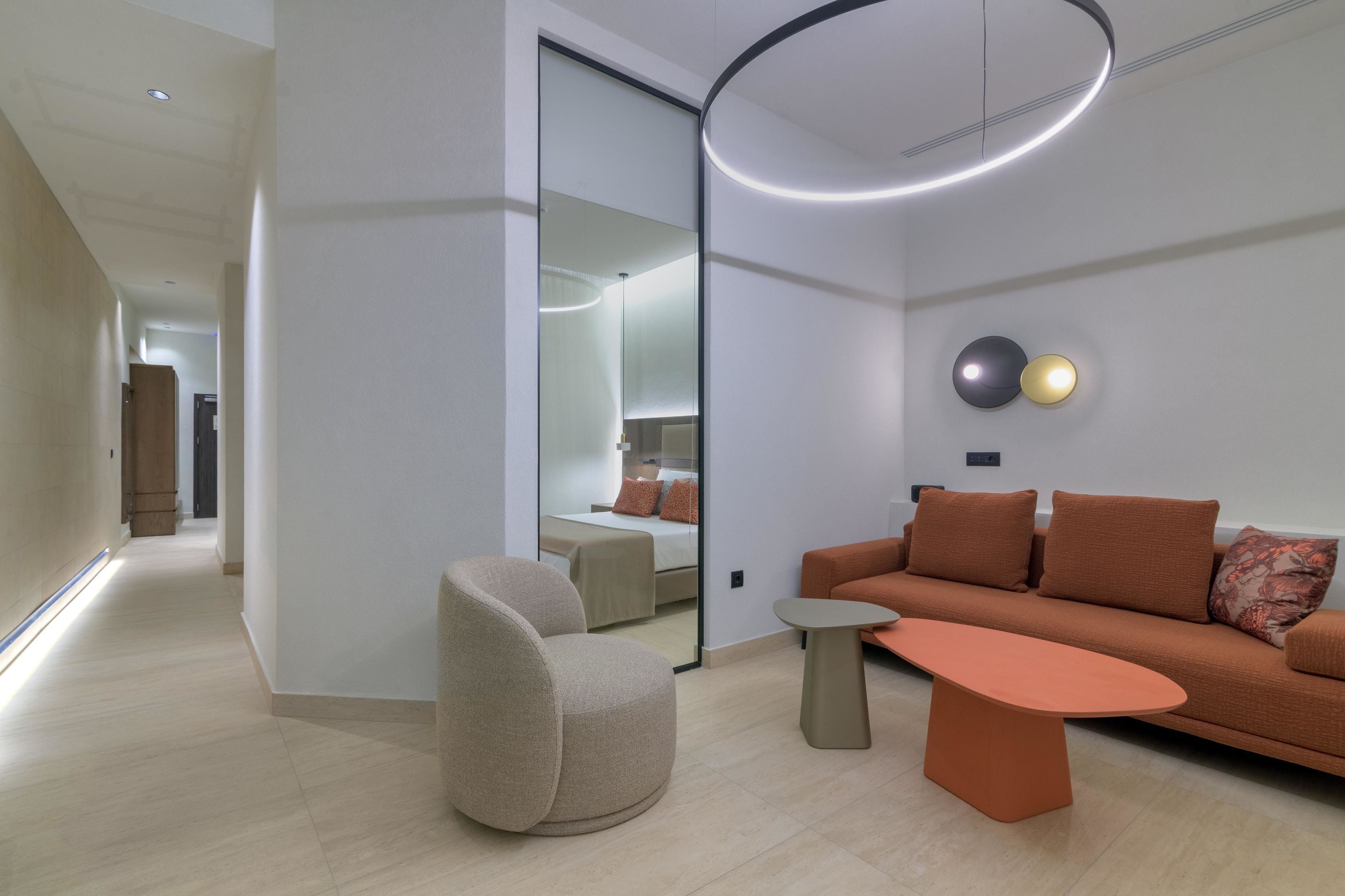 Una sala de estar moderna con sofá, sillón y mesa de centro, que presenta un espejo grande y una lámpara circular.