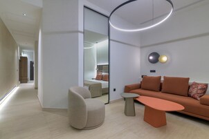 Una sala de estar moderna con sofá, sillón y mesa de centro, que presenta un espejo grande y una lámpara circular.