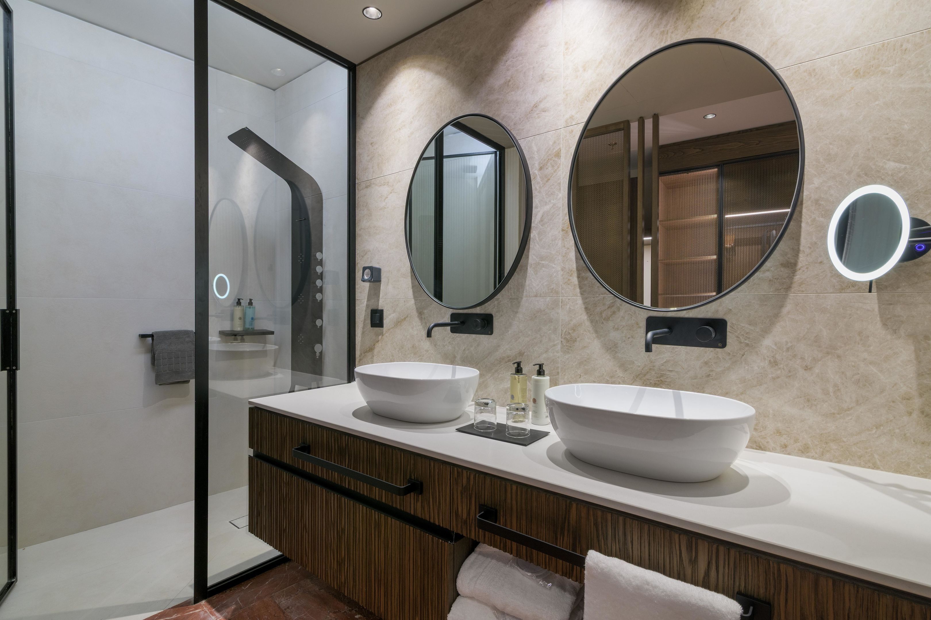 A modern bathroom with two large white sinks, a glass shower enclosure, and a mirror with a built-in light.