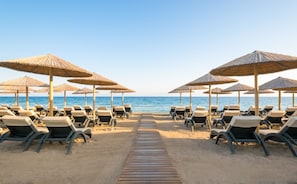 A beach with rows of sun loungers and thatched umbrellas, leading to the sea.