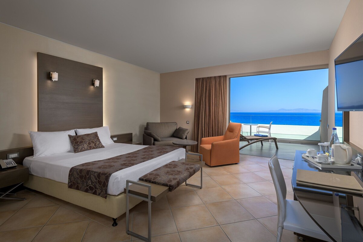 Een hotelkamer met een bed, een bureau, een stoel en uitzicht op de oceaan.