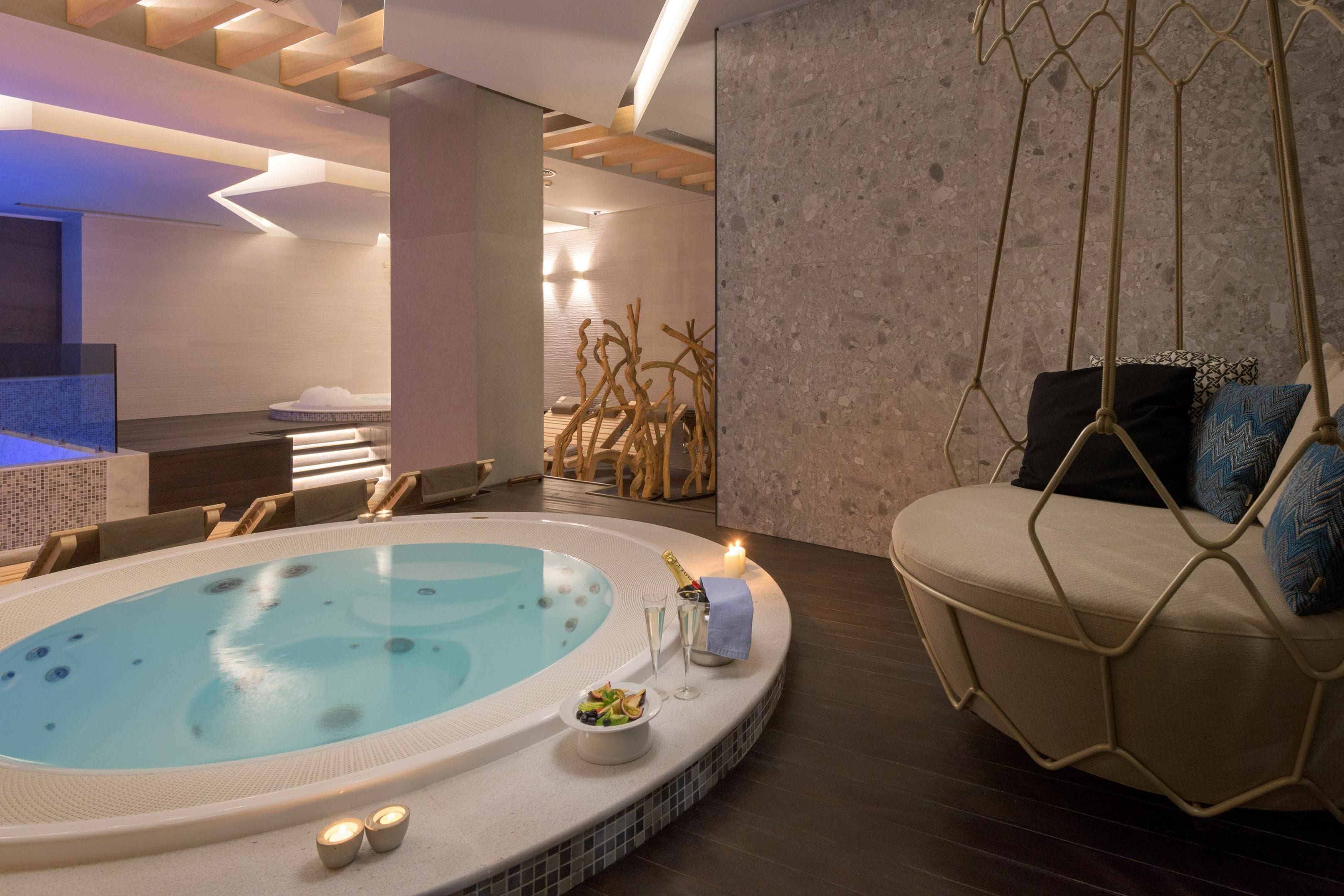A modern spa area with a hot tub, seating, and a relaxation area with a hanging chair.