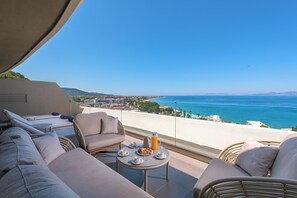 Ein Balkon mit Meerblick, ein Sofa, ein Tisch mit Frühstücksgebäck und ein Stuhl.