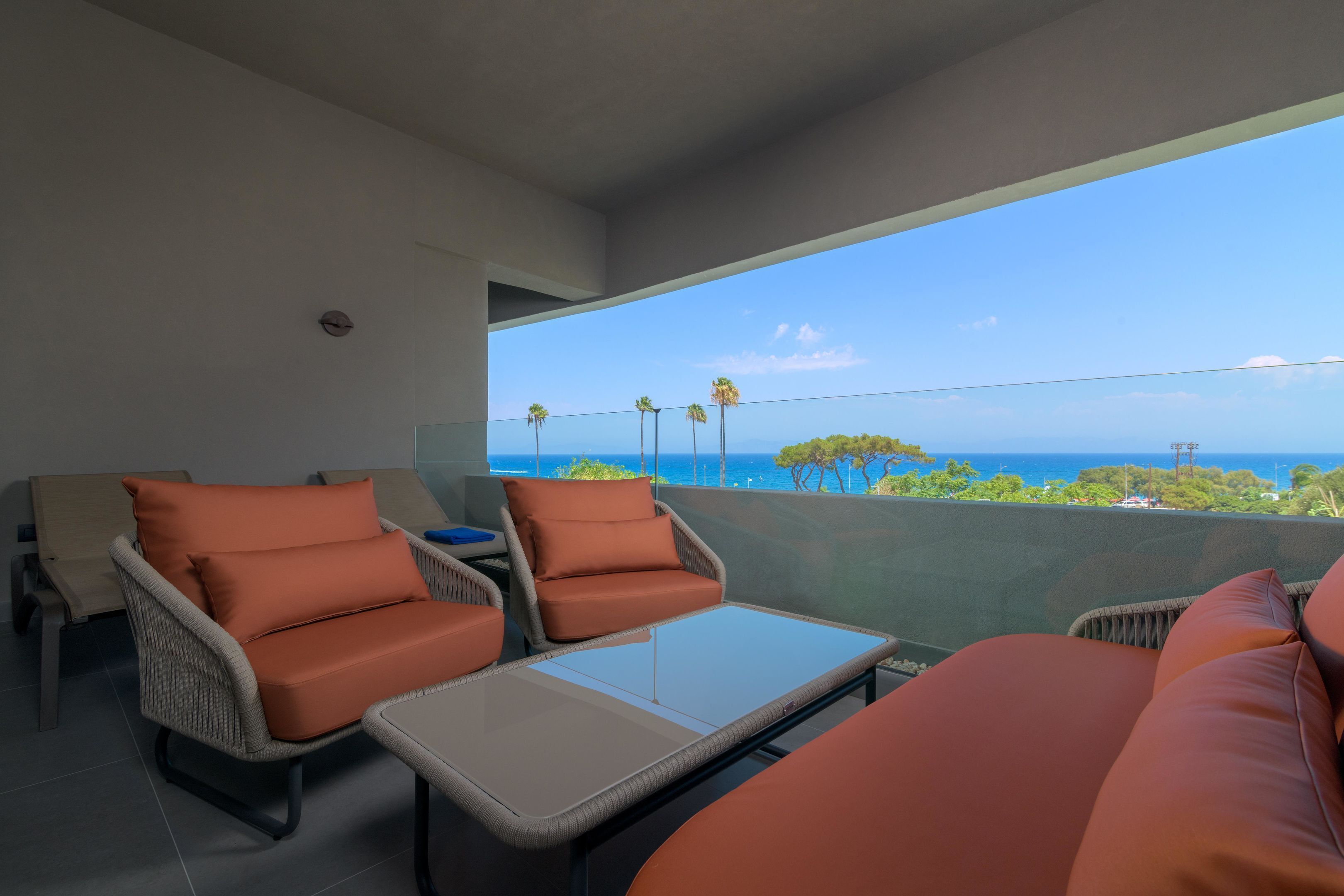 A balcony with wicker furniture, a glass table, and a view of the sea.