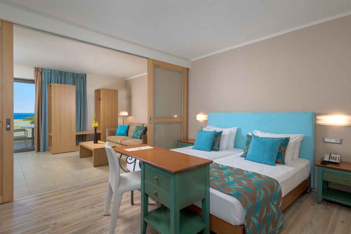 Een moderne hotelkamer met een groot bed, een bureau en een stoel. Door het raam is er uitzicht op zee.