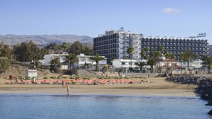 A hotel with multiple floors, a beach in the foreground, and mountains in the background. - Relaxia Beverly Park (San Bartolomé de Tirajana)