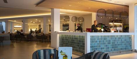 A modern hotel lobby with a bar area, seating arrangements, and a tiled backsplash.