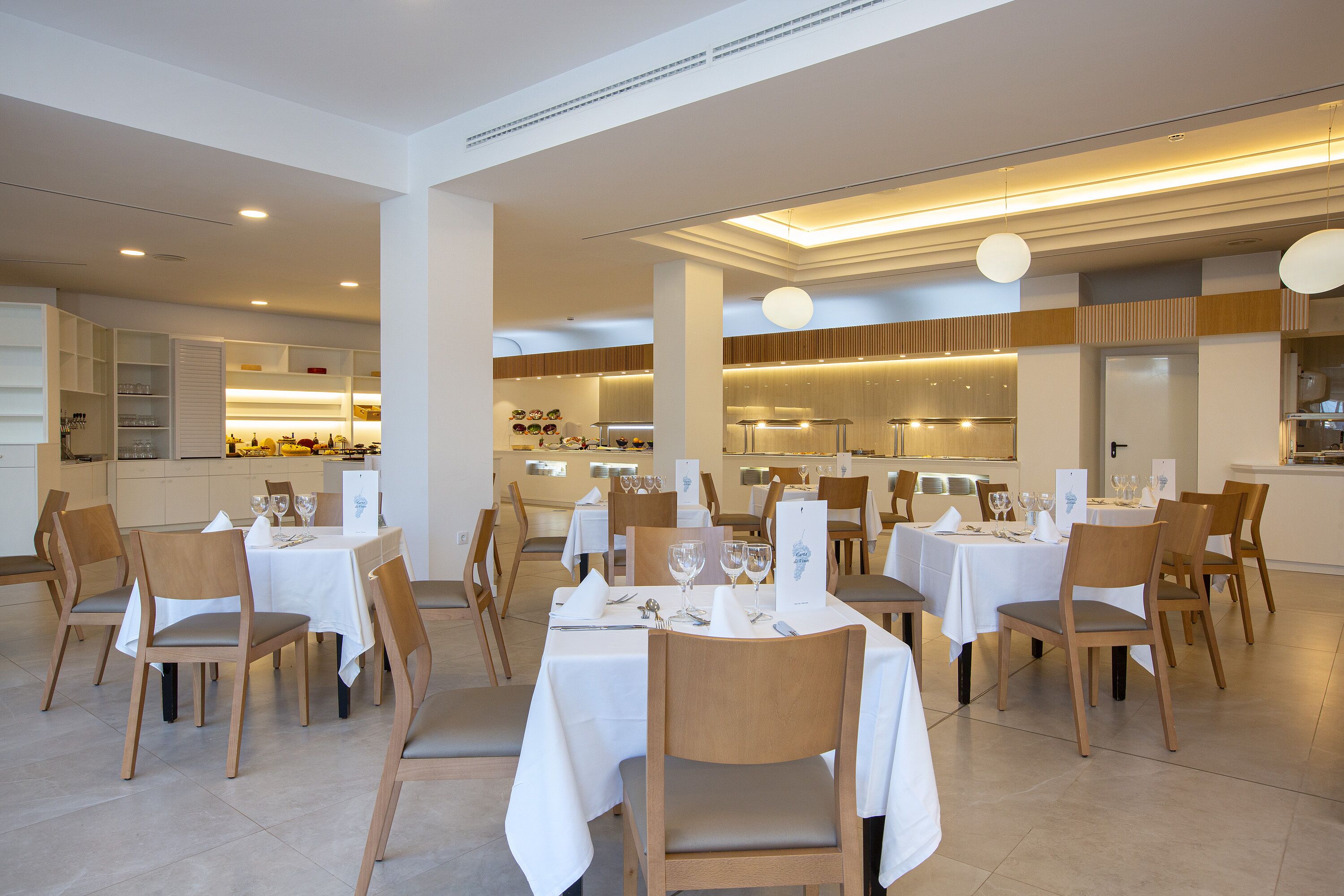 Un restaurante con varias mesas y sillas, una cocina al fondo y un interior limpio y moderno.