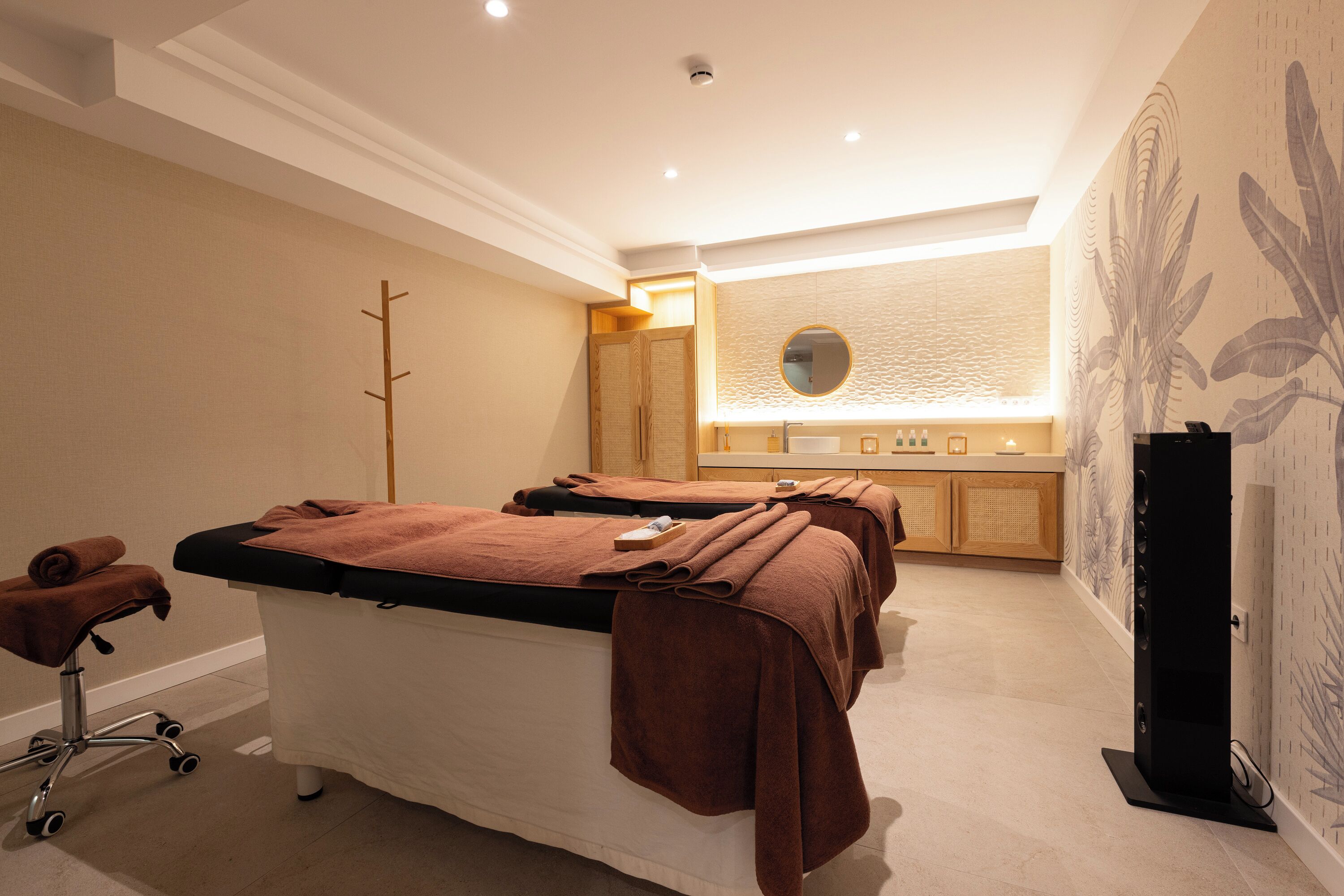 Une salle de spa équipée de tables de massage, d’un comptoir d’accueil et d’un mur orné d’un motif de feuilles tropicales.