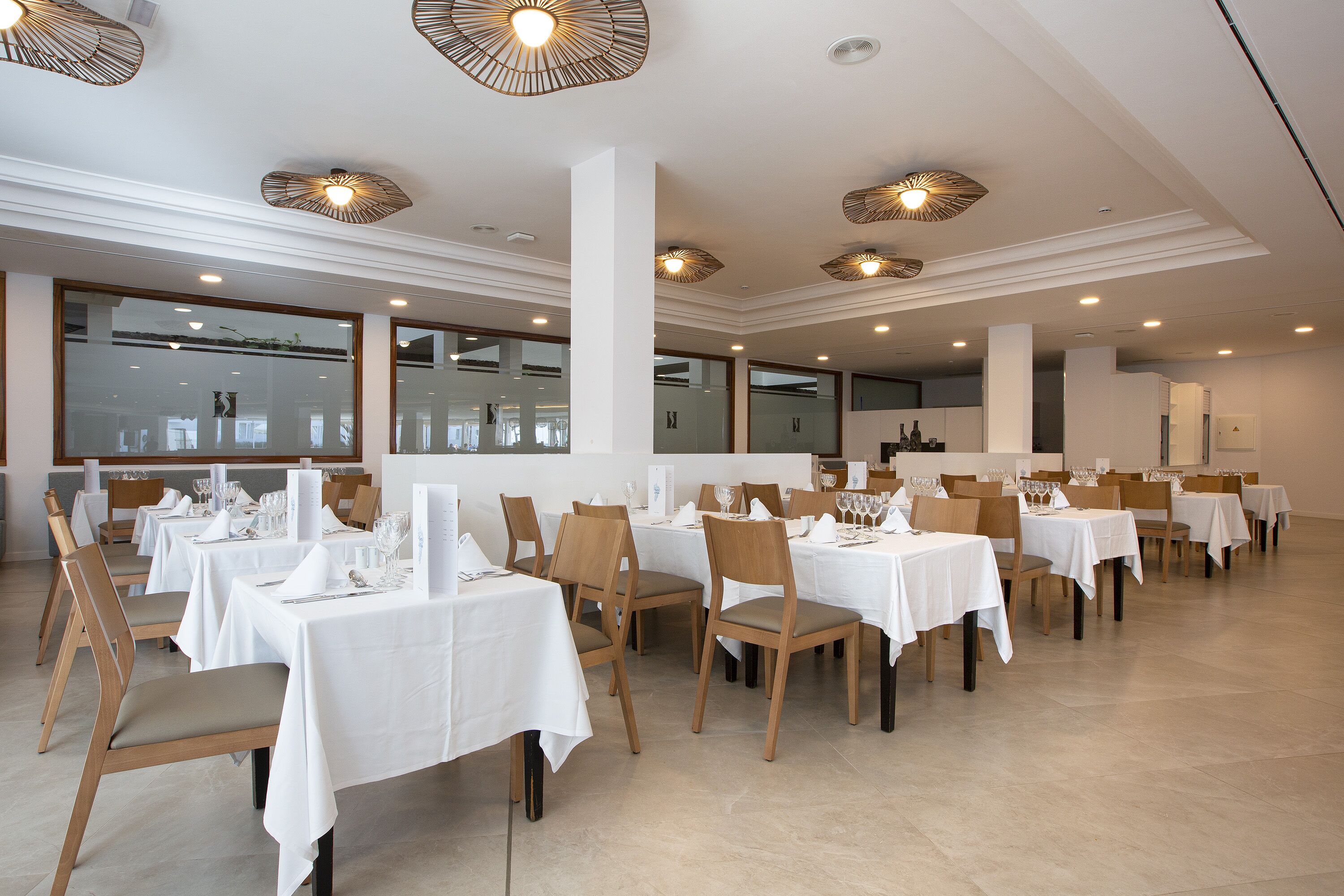 Un espace repas avec des tables dressées, des chaises en bois et des luminaires modernes au plafond.