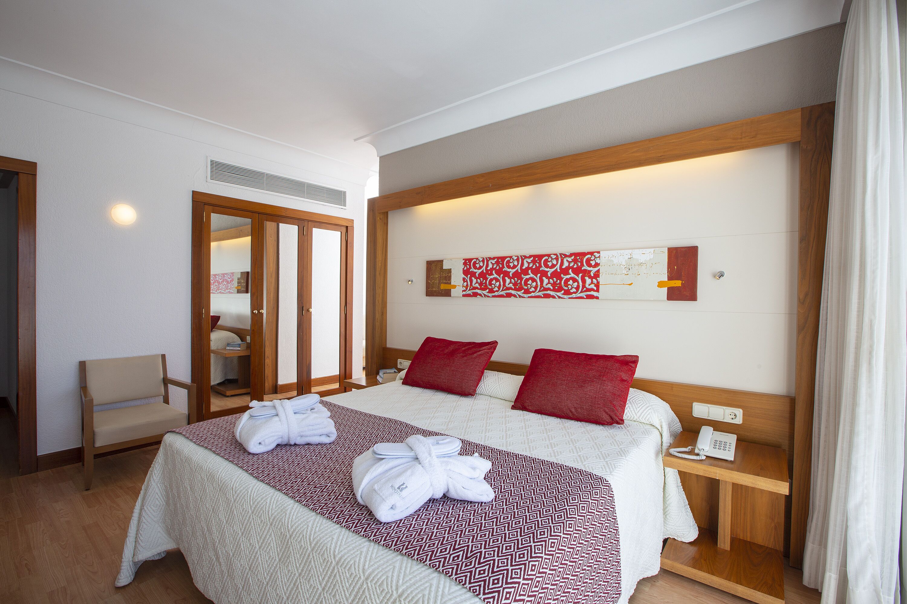 A hotel room with a large bed, a wooden headboard, a bedside table with a phone, and a mirror.
