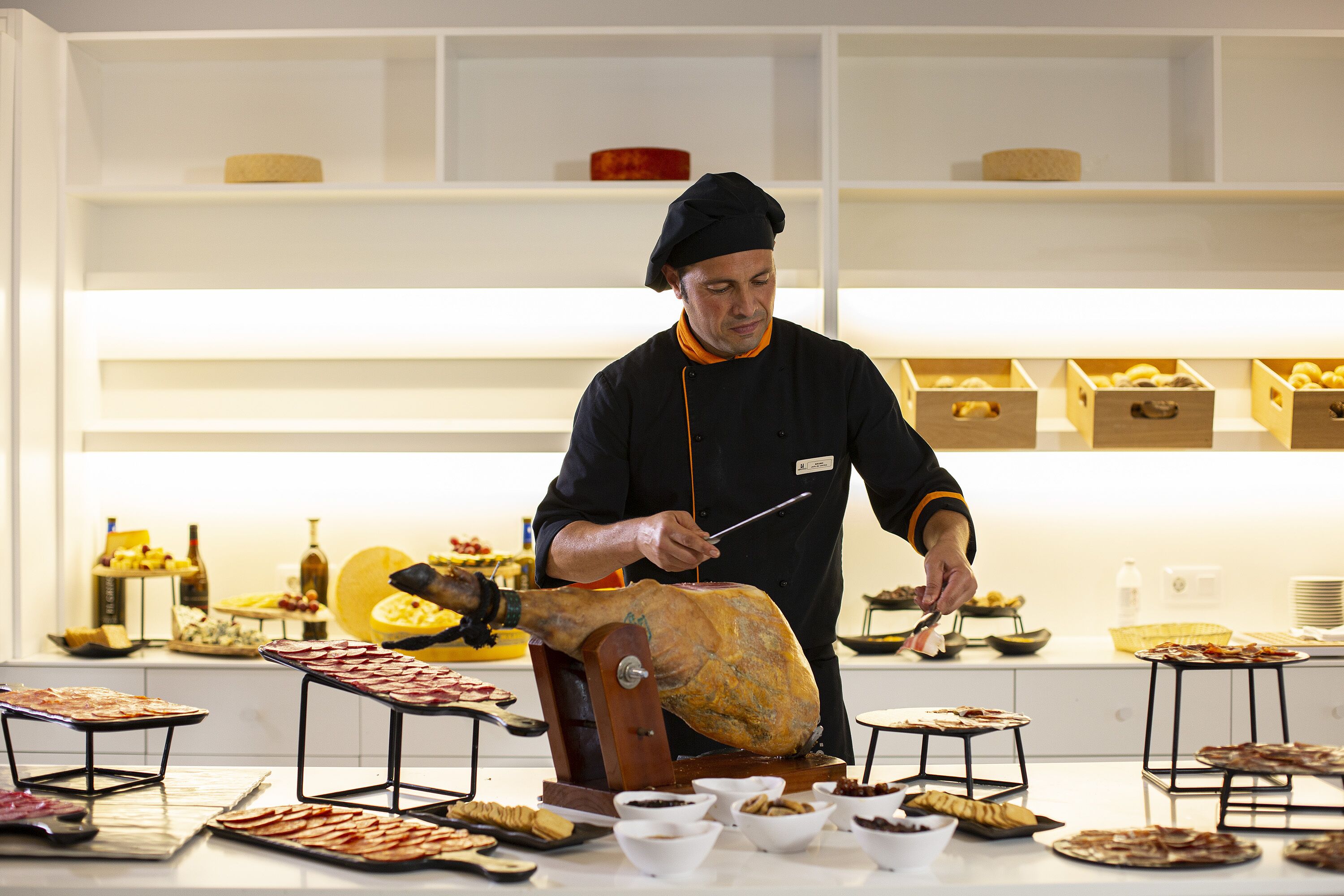 Een kok snijdt een groot gebraden varken in een moderne keuken, met diverse etenswaren en keukengerei op het aanrecht.