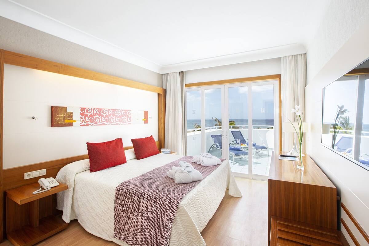 A hotel room with a large bed, a desk with a phone, and a view of the sea.
