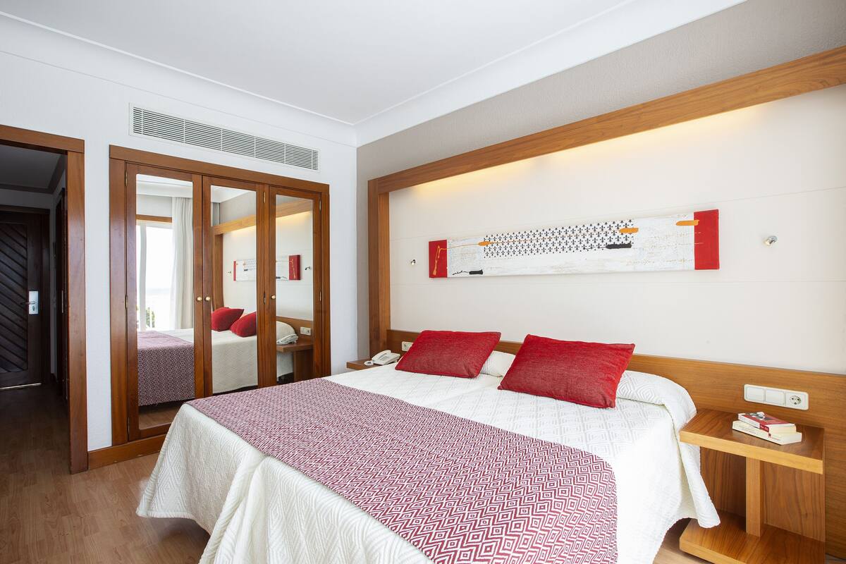A hotel room with a bed, a bedside table, a mirror, and a wardrobe.