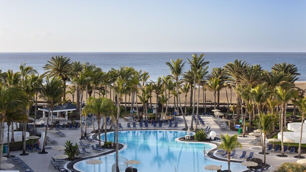 A resort pool area with palm trees, lounge chairs, and a view of the ocean. - Hipotels La Geria (Tías)