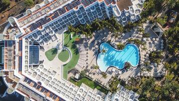 An aerial view of a cruise ship with multiple decks, including a pool area with two swimming pools and sun loungers.