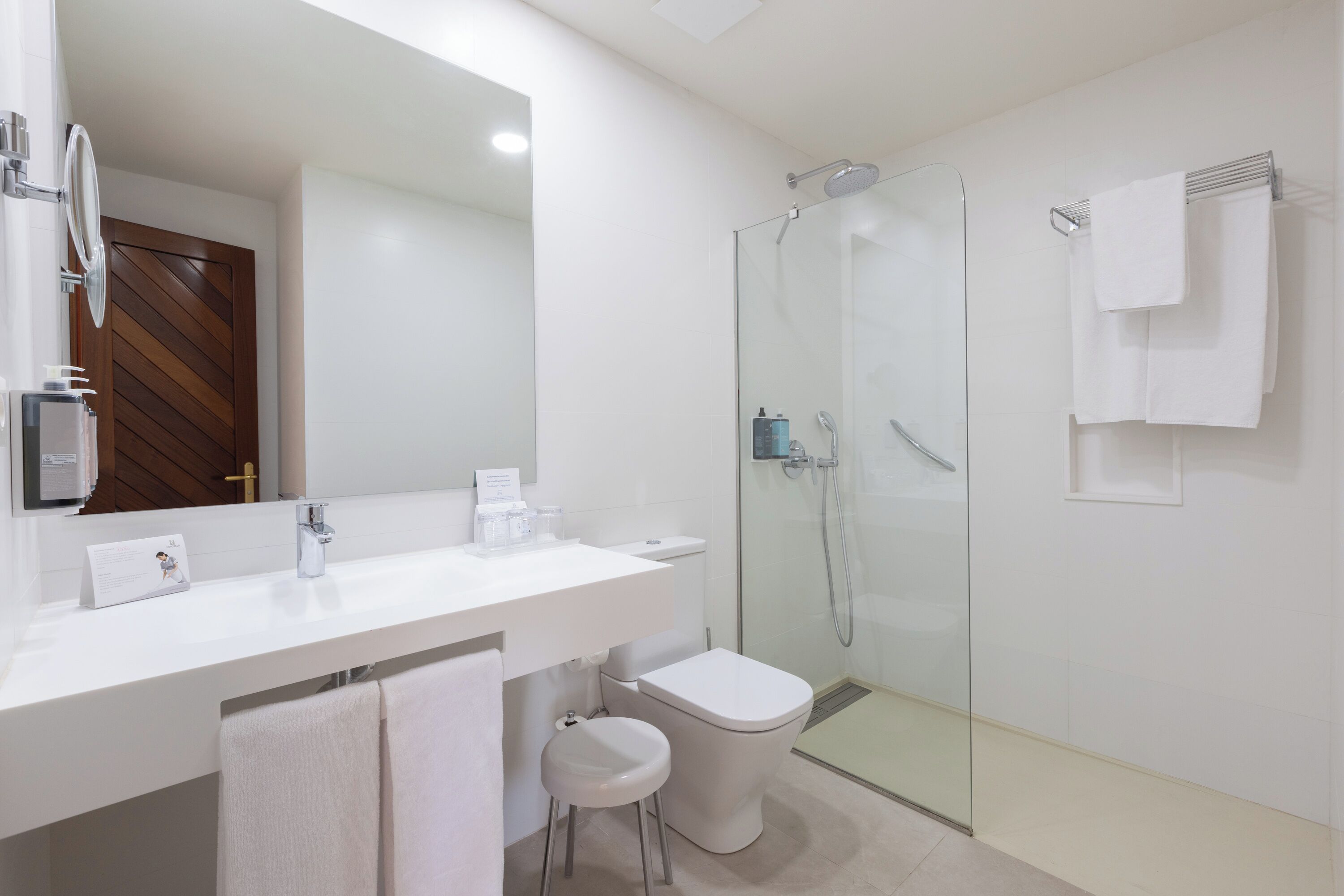 A modern bathroom with a white vanity, a glass shower enclosure, and a wooden door.