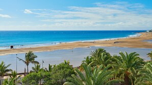A beach with clear blue water, sandy shore, and palm trees. - Hipotels La Geria (Tías)