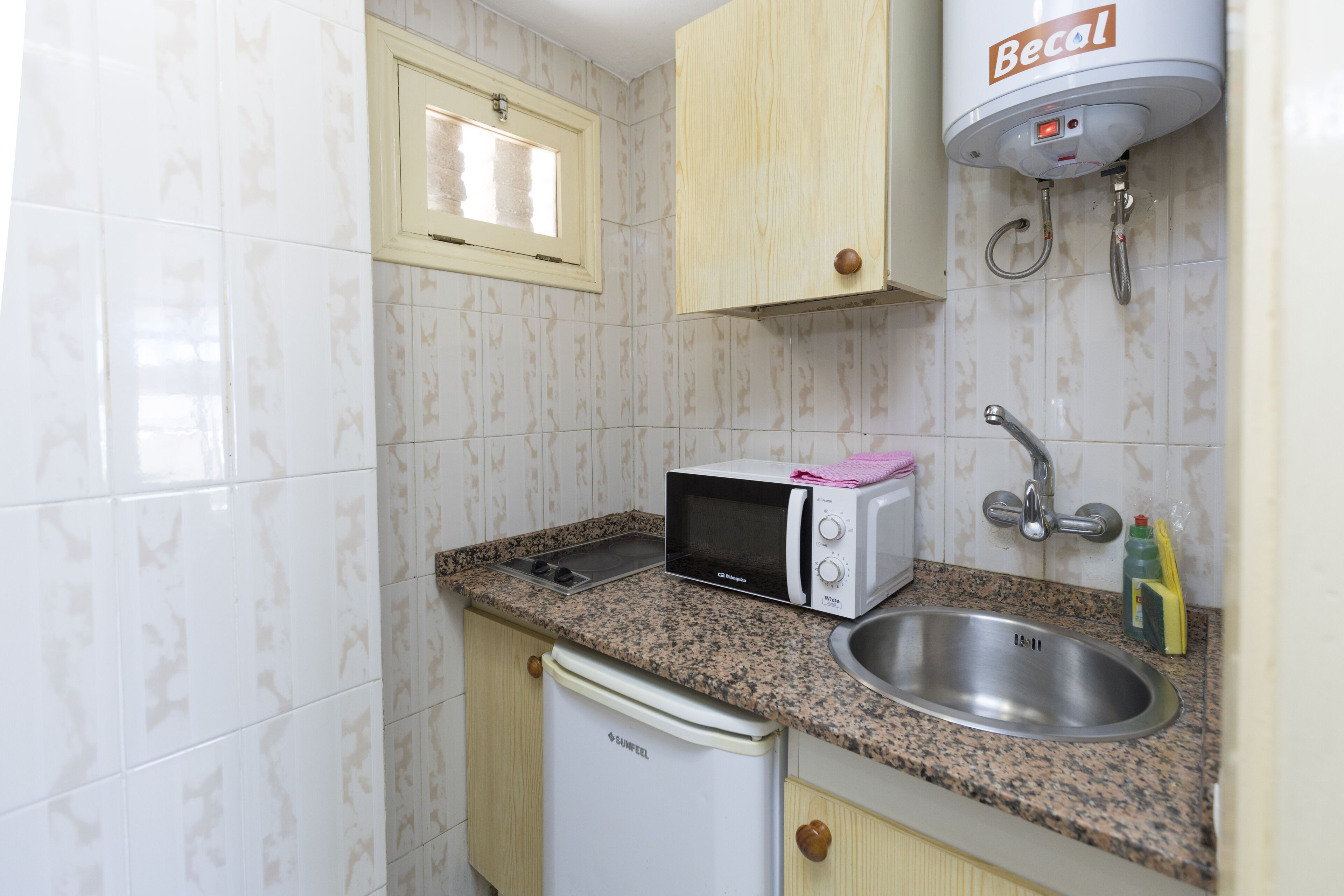 A compact kitchen with a microwave, sink, and a water heater.
