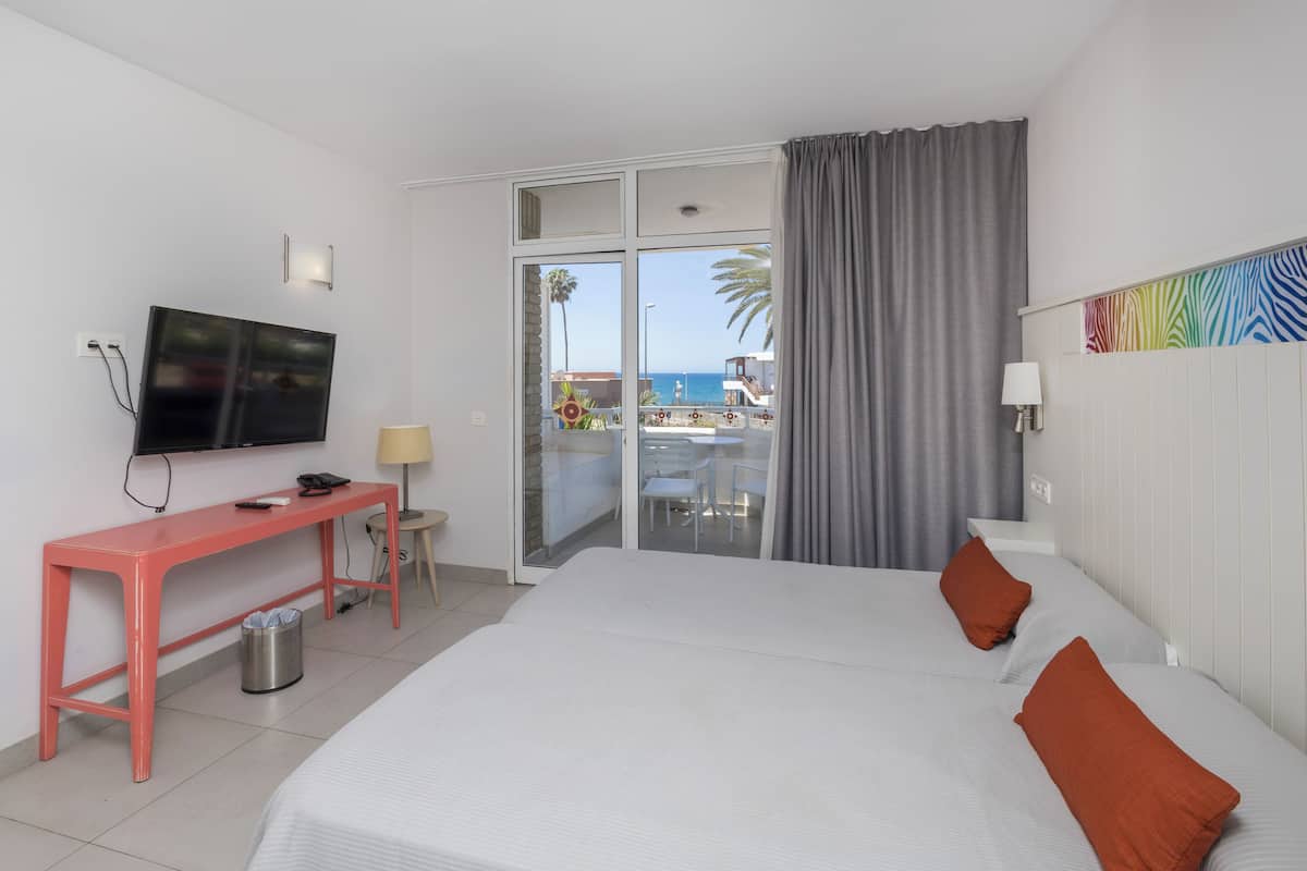 Une chambre d’hôtel avec un lit, un bureau, une télévision et vue sur la plage.