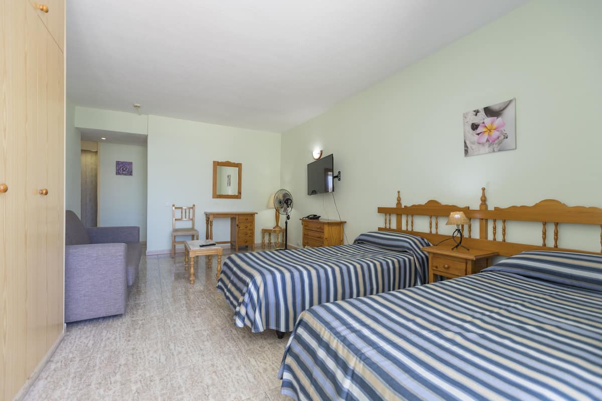 Une chambre d’hôtel avec deux lits simples, une table de chevet en bois, un bureau avec une chaise et un téléviseur fixé au mur.