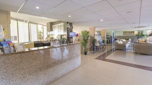 Un vestíbulo de hotel con mostrador de recepción, zona de estar y un reloj en la pared.