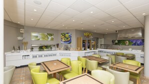 Un restaurante con varias mesas y sillas, una zona de cocina y decoración en las paredes.