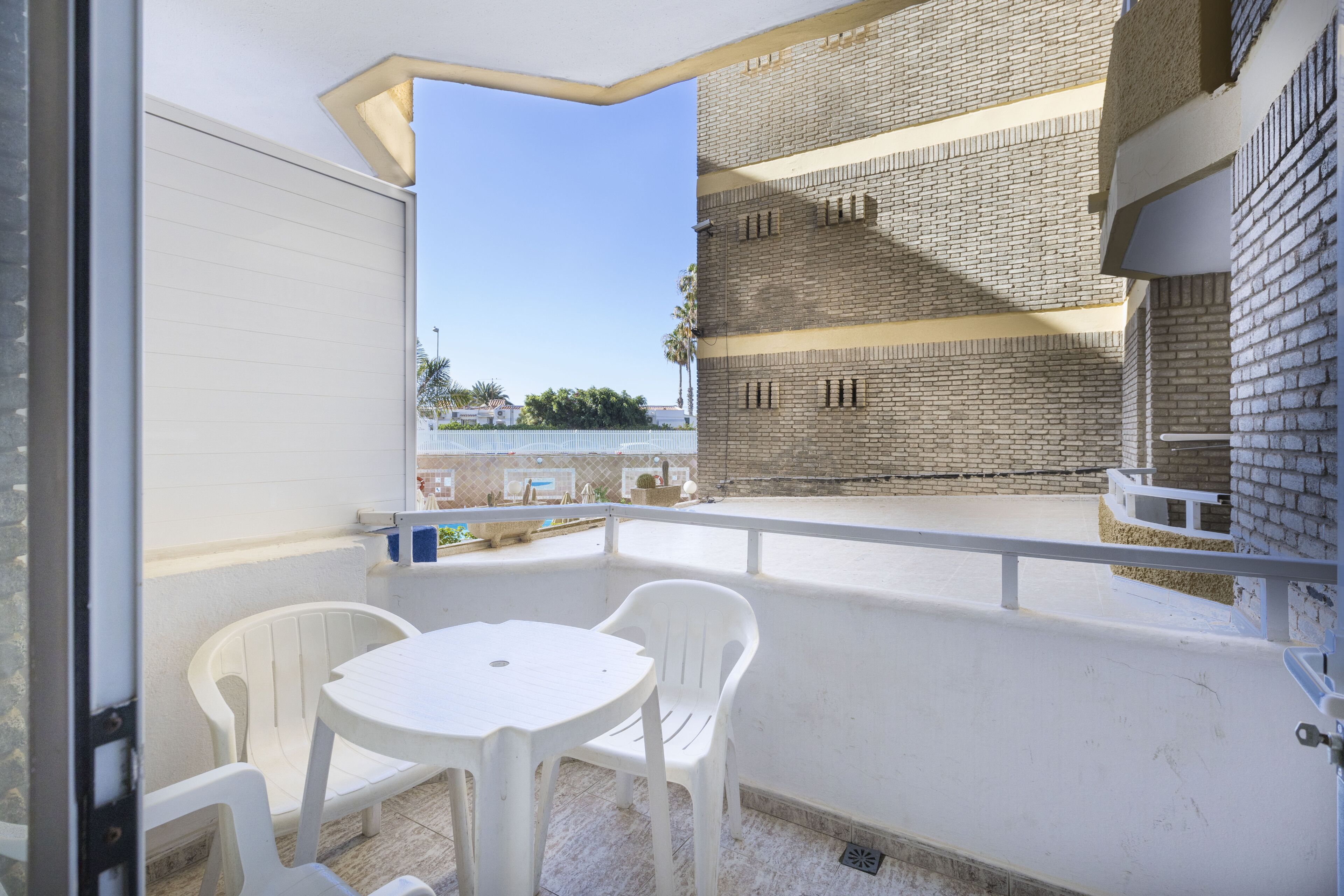 Un balcon avec une table et des chaises blanches, un mur de briques et une vue dégagée sur les environs.