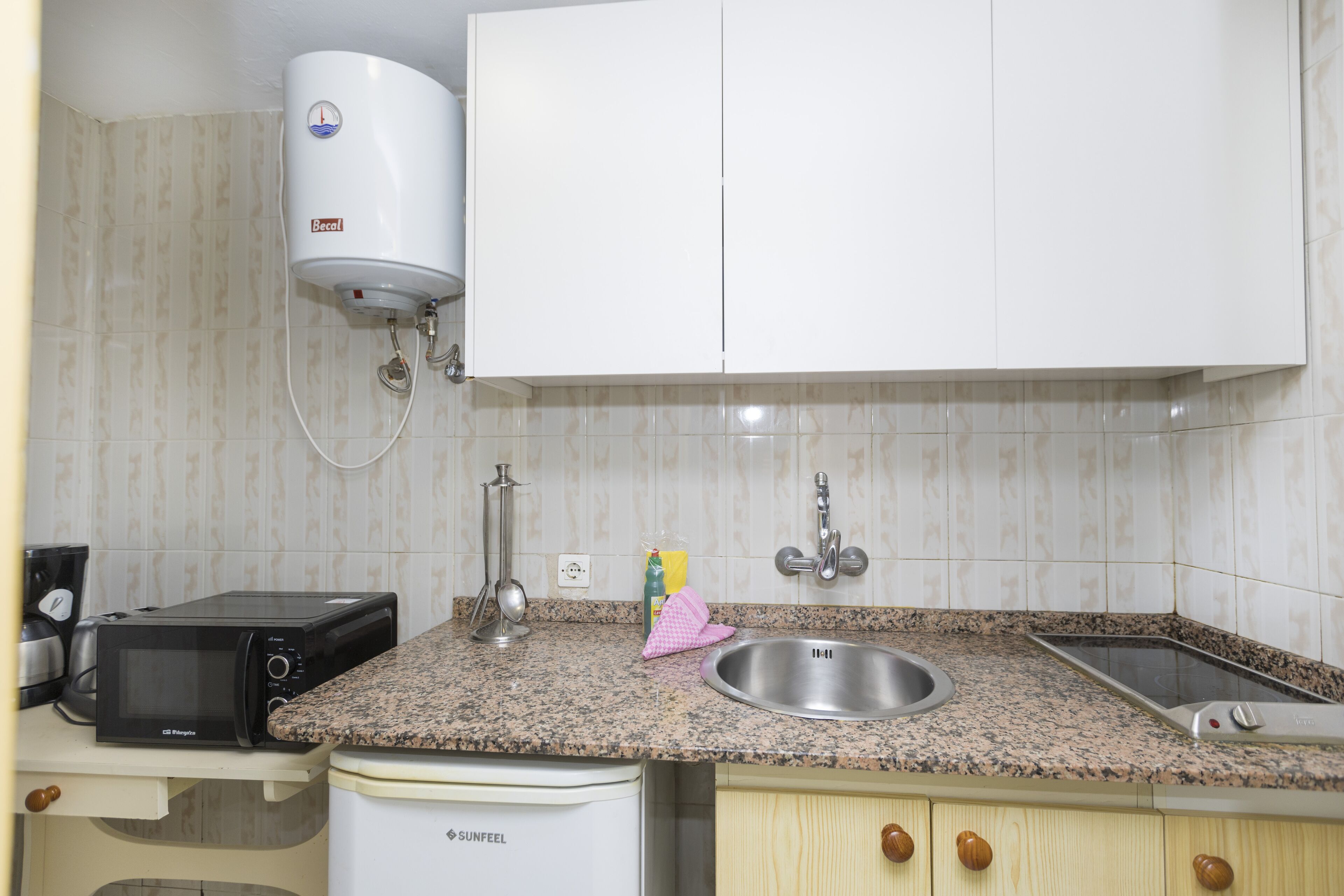A kitchen with a microwave, toaster, sink, and a water heater.