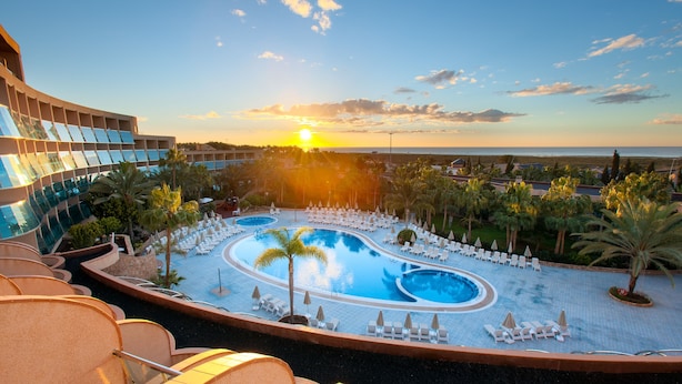 Un resort con una piscina grande, tumbonas y vistas a la puesta de sol sobre el océano.