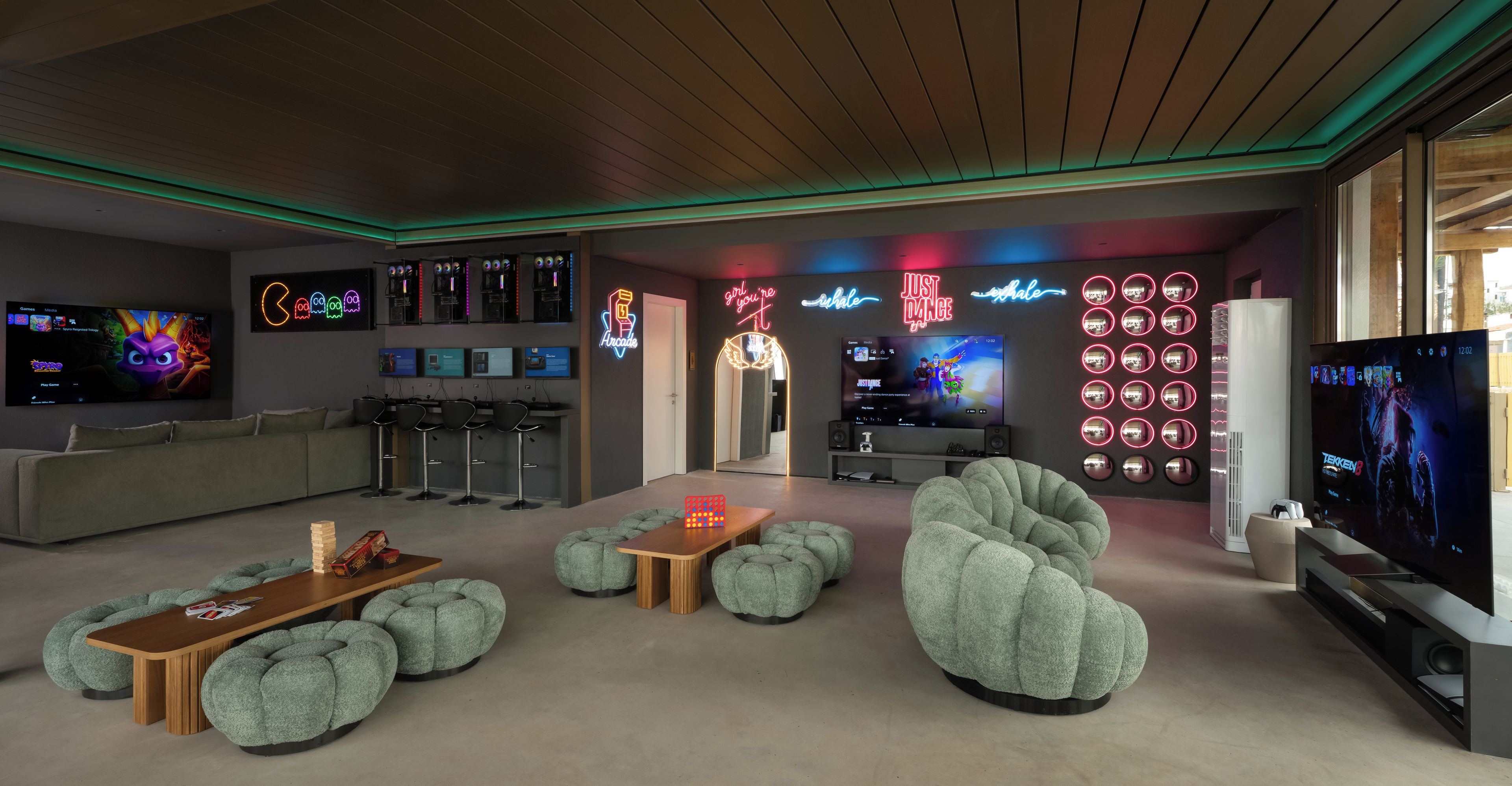 A modern living room with a gaming setup, including multiple screens and neon signs.