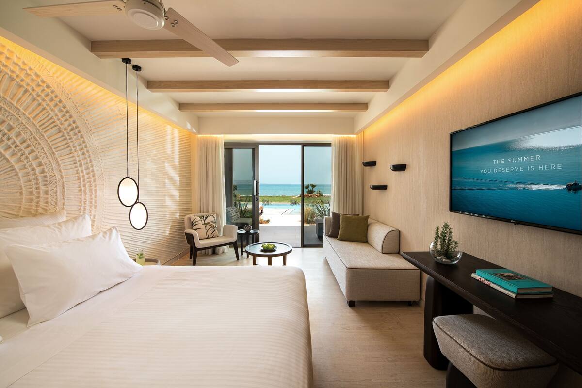 Une chambre d’hôtel moderne dotée d’un grand lit, d’un canapé, d’une télévision et offrant une vue sur la mer.