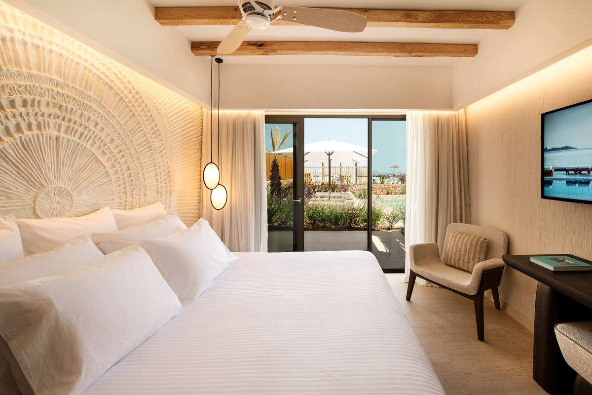 Une chambre avec un grand lit, une chaise, un téléviseur et une vue sur l’extérieur.