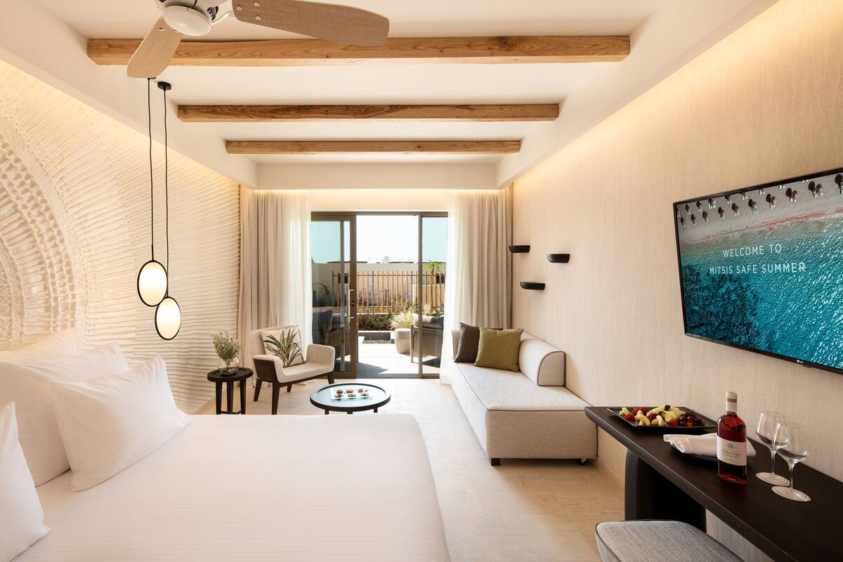 Une chambre d’hôtel moderne avec un lit, un canapé, une petite table et un téléviseur fixé au mur.