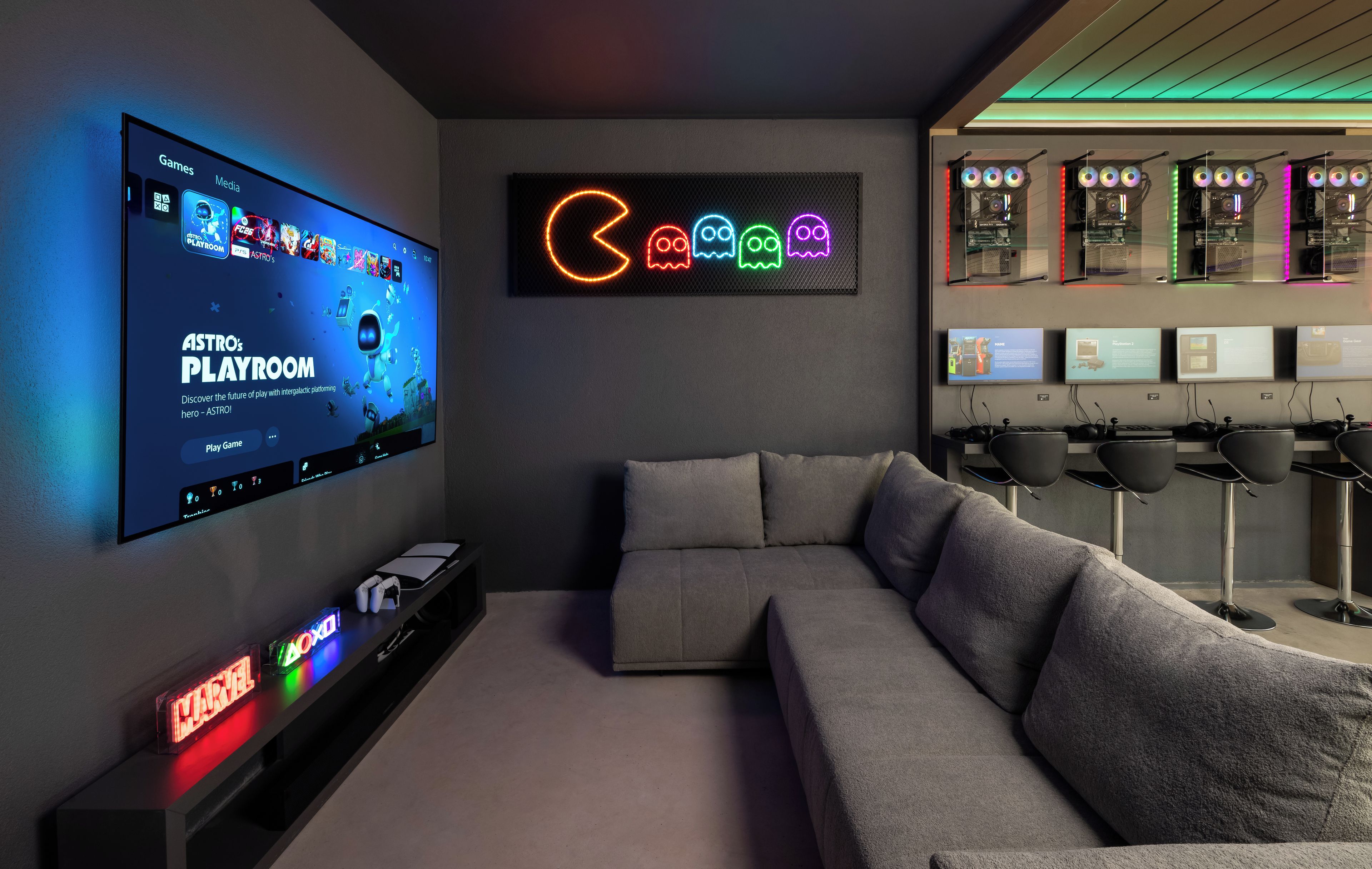 A modern gaming room with a large TV displaying a game, a neon sign, and a gaming PC setup.