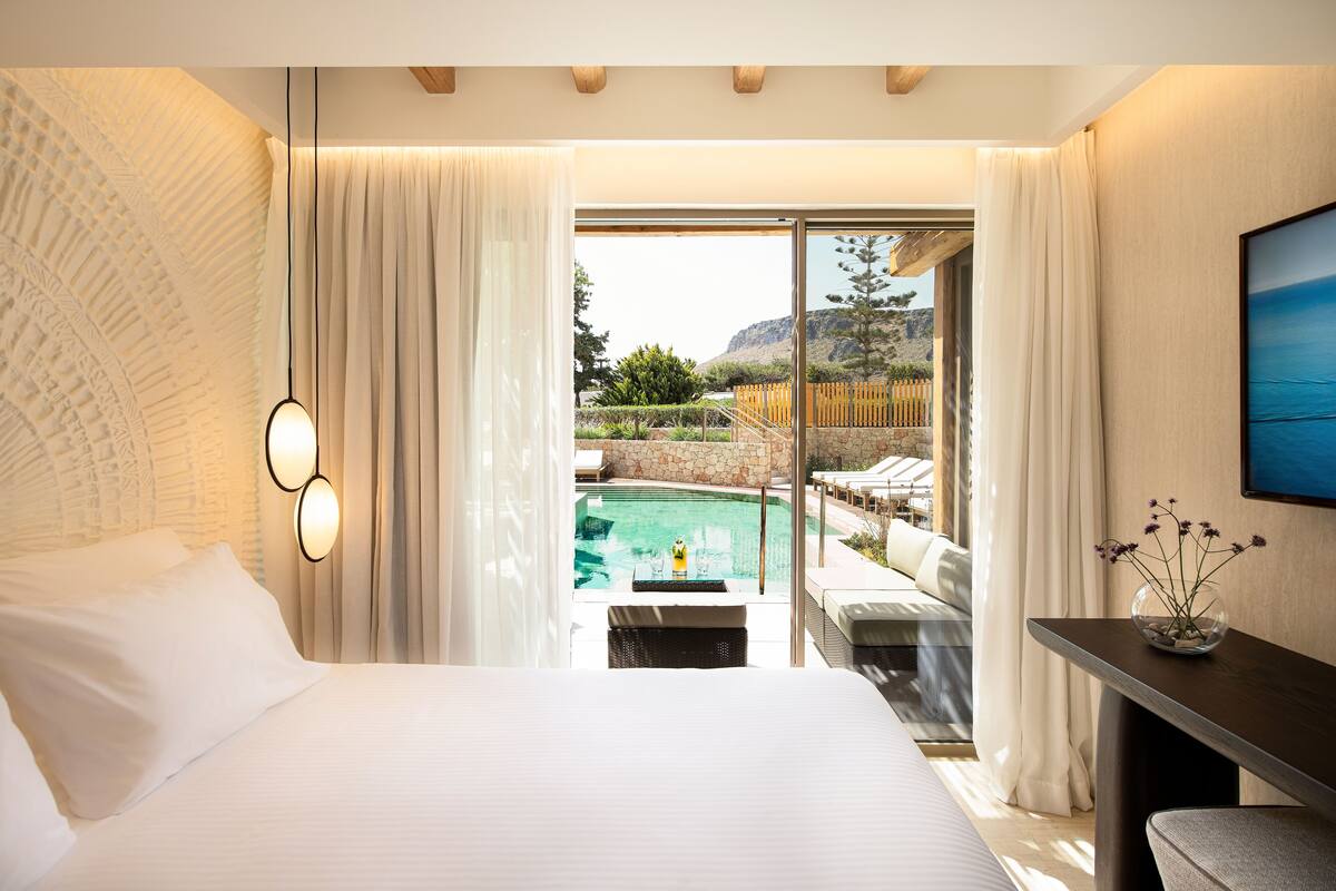 Une chambre dotée d’un grand lit, offrant une vue sur une piscine, et comprenant un coin repas avec une table et des chaises.