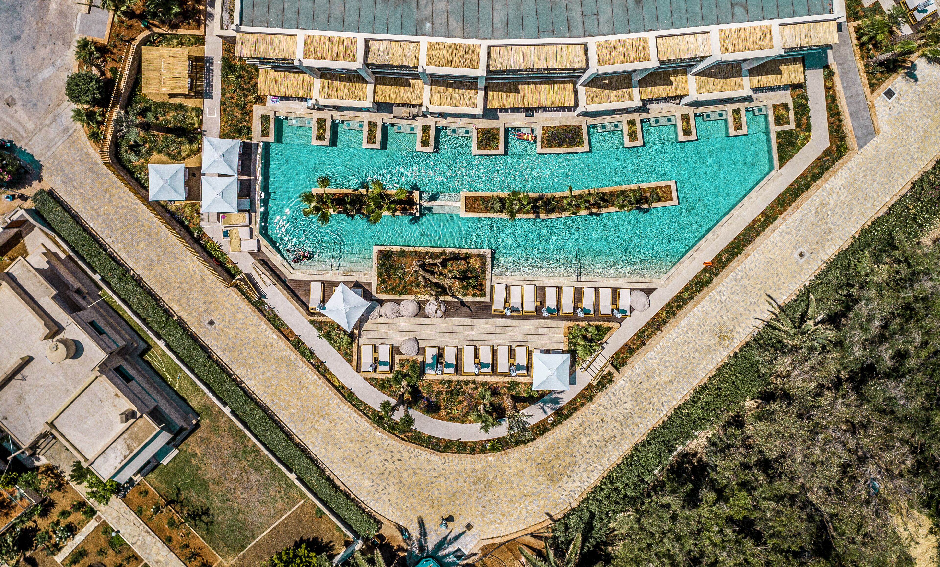 An aerial view of a resort with a large central pool, multiple sun loungers, and a surrounding landscaped area.