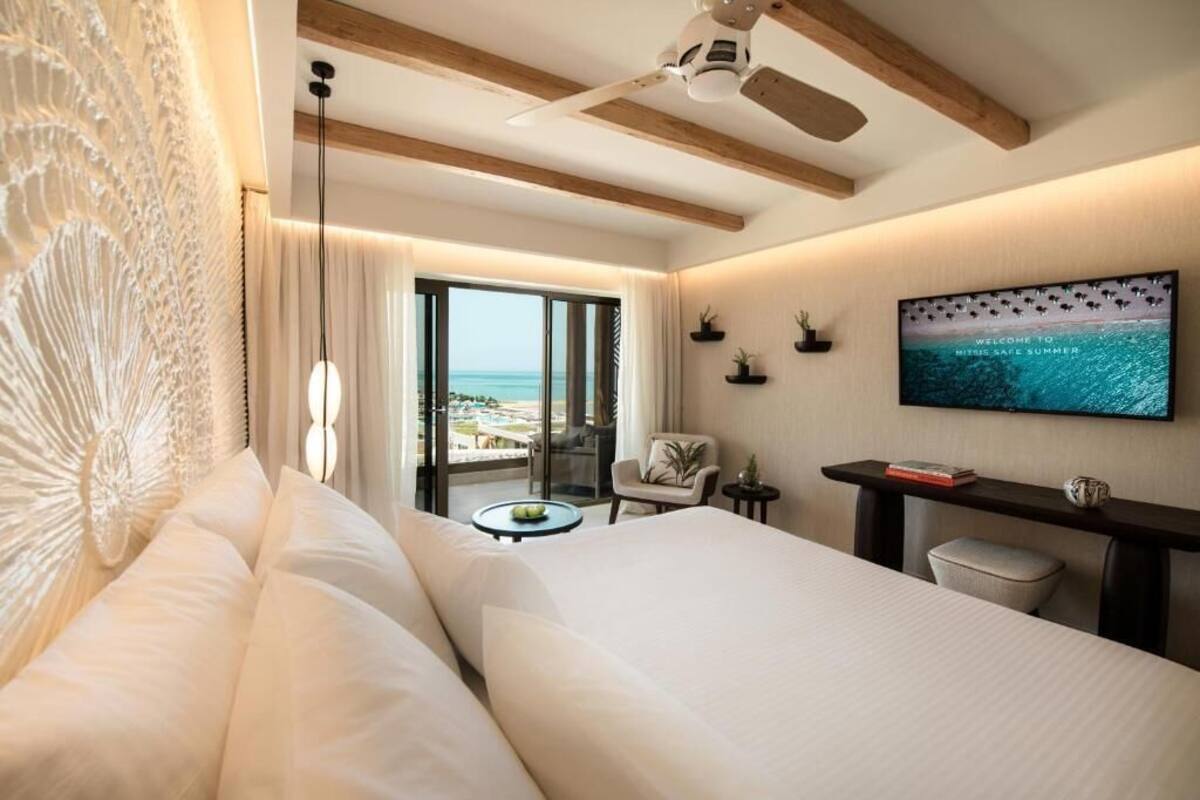 Une chambre d’hôtel comprenant un lit, un bureau, une chaise, une télévision et un balcon avec vue sur la mer.