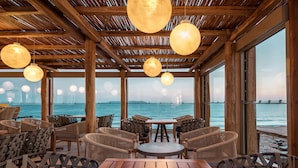 A wooden deck with wicker furniture and hanging spherical lights, overlooking a body of water with a distant bridge. - Mitsis Selection Rinela (Hersonissos)