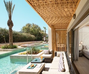 A poolside area with a lounge chair, a table with a drink, and a view of a pool and greenery.