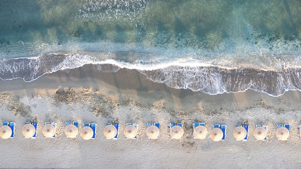 A beach with waves approaching the shore, and rows of beach umbrellas aligned along the sand. - Pigale Beach Resort (Kusadasi)