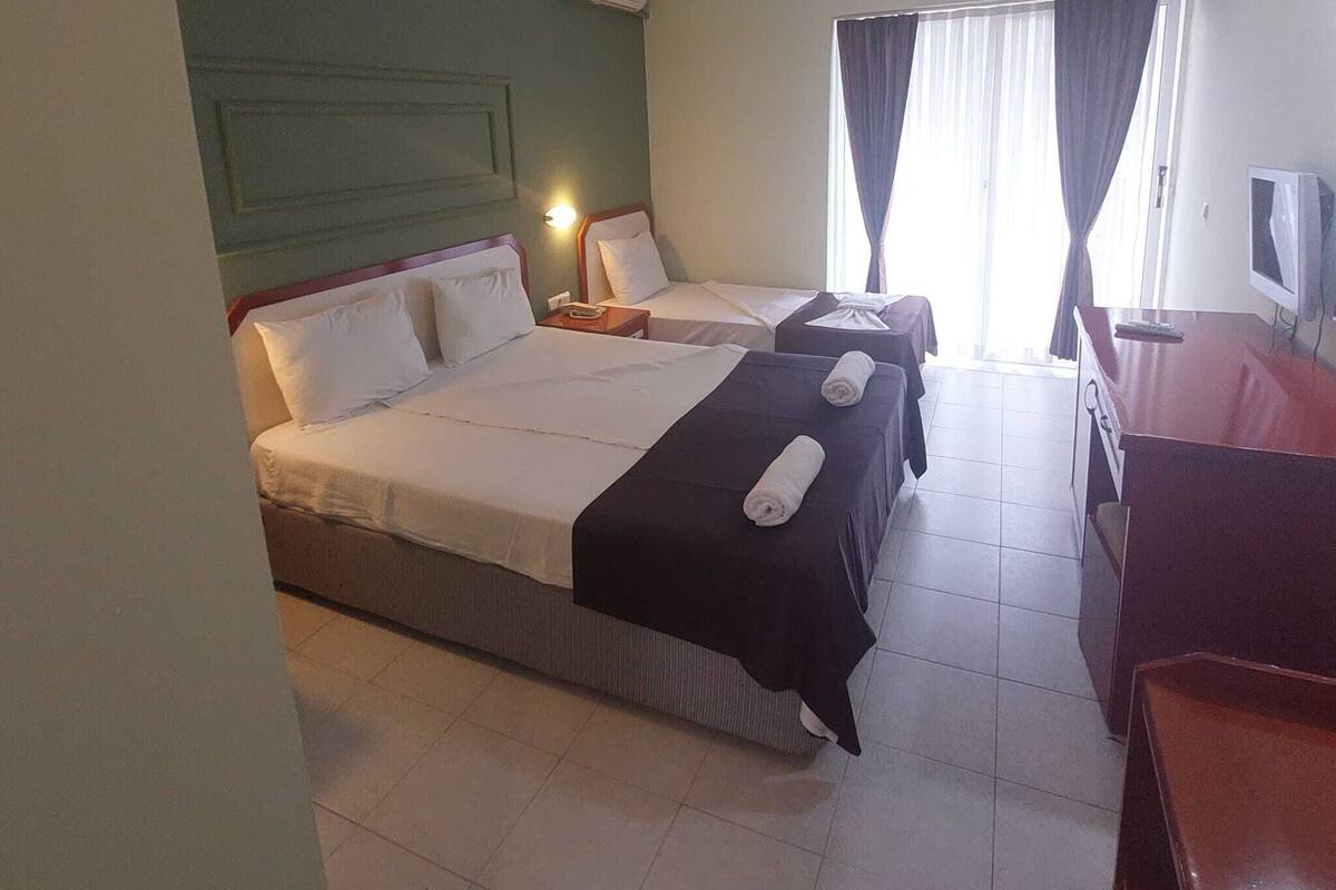 A hotel room with two beds, a desk, a TV, and a window with curtains.