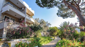 A residential building with balconies, a paved pathway, and lush greenery. - Pigale Beach Resort (Kusadasi)