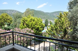 A balcony with a view of a mountainous landscape, a pool, and surrounding greenery. - Pigale Beach Resort (Kusadasi)