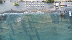 An aerial view of a beach with rows of sun loungers and umbrellas, a small building with a roof, and a few boats. - Pigale Beach Resort (Kusadasi)