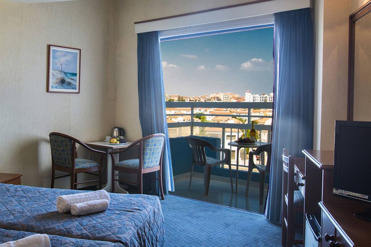 Hotellihuone, jossa on sänky, työpöytä, tuoli, televisio ja parveke, jolta on näkymä kaupunkiin.